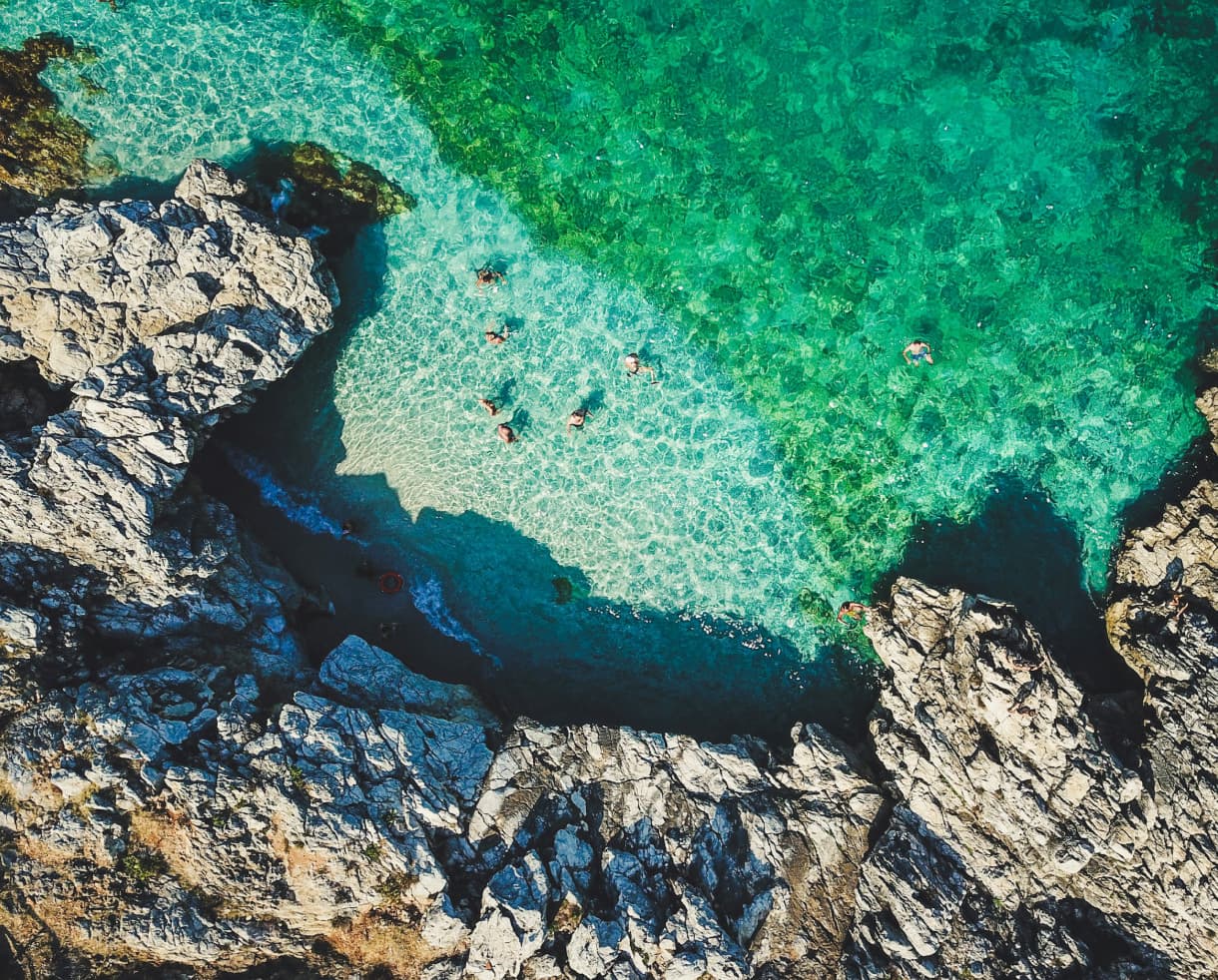 Swimmers in a clear, rocky cove, seen from above